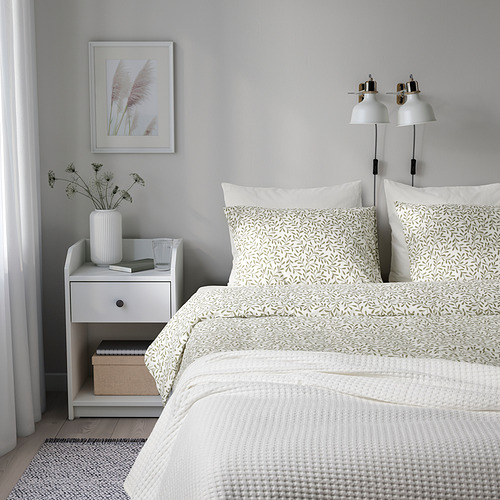 Dormitorio minimalista con edredón de hojas de somnol, paredes blancas, mesita de noche, jarrón, lámparas sobre la cama, sensación de naturaleza tranquila.