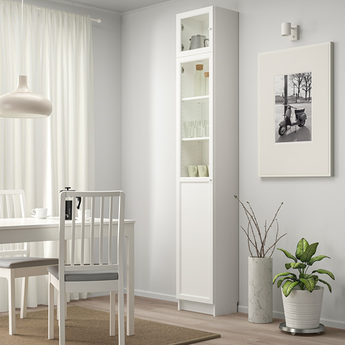 Área de comedor minimalista con un gabinete BILLY blanco que exhibe artículos, junto a una silla y mesa blancas debajo de una lámpara colgante.