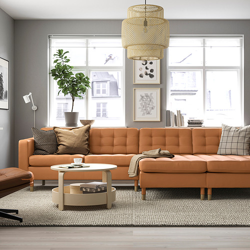 Sala de estar moderna con un gran sofá naranja en forma de L, mesa de centro de madera, alfombra elegante, planta alta y grandes ventanales.