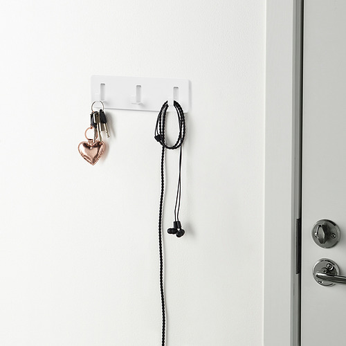 La pared blanca sostiene llaves y auriculares con ganchos autoadhesivos.