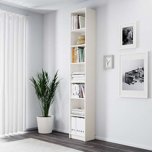 Rincón minimalista con librería blanca BILLY, llena de libros y plantas. Los estantes altos y ajustables exhiben los artículos de manera ordenada.