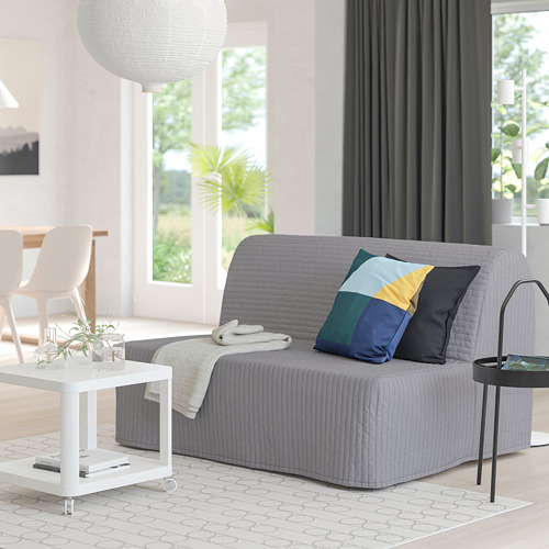 Sala de estar moderna con sofá cama gris, almohadas de colores, mesa de centro blanca, cortinas grises y gran ventanal.