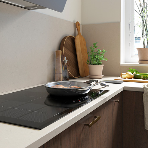 Cocina moderna con elegante estufa de inducción negra, utensilios de madera, plantas y productos frescos en el mostrador.