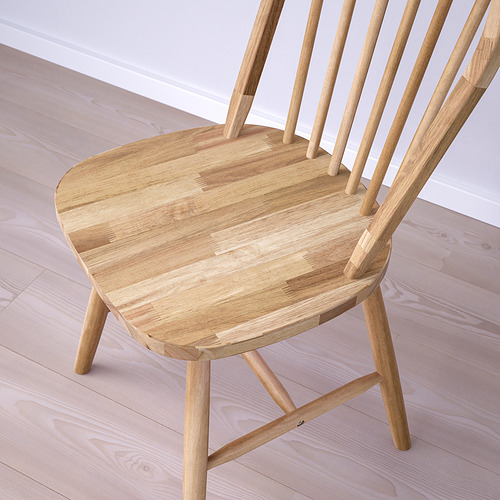 Silla de madera ligera con un asiento liso y curvo y un delgado respaldo de huso, colocada sobre un suelo de madera a juego.
