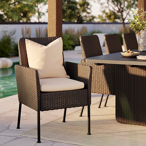 Silla de mimbre VITTSKÄR marrón con cojines beige, parte de un patio situado cerca de una piscina.