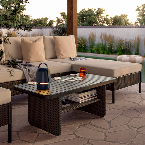 Patio con sofá VITTSKÄR beige, mesa de centro, libros, taza y linterna sobre suelo de piedra.