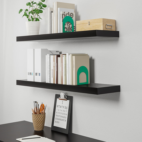 Estantes LACK NEGROS montados en la pared que contienen libros, plantas y decoración; Escritorio de abajo con calendario y bolígrafos.