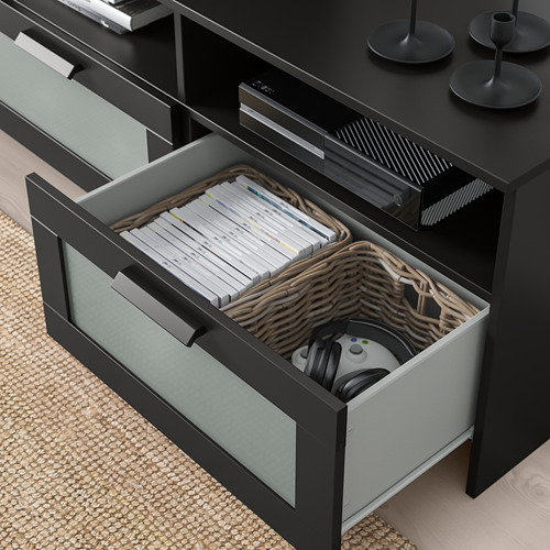 El cajón abierto del soporte de TV revela juegos organizados, controles remotos y una canasta tejida que contiene accesorios de juego.