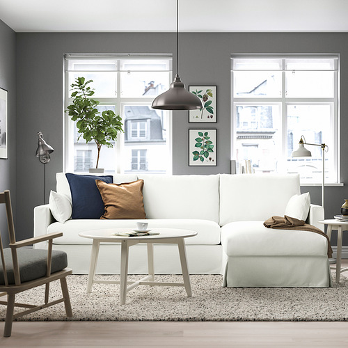 Salón moderno con sofá blanco, pared oscura, grandes ventanales, lámpara colgante, mesa de centro redonda, silla gris con cojín beige.
