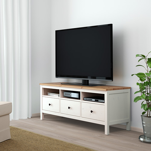 Mueble de tv HEMNES con televisor de pantalla plana, cajones y estante entre cortinas y una planta.