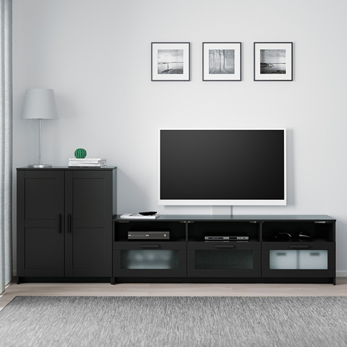 Moderna configuración de televisor BRIMNES negro con gabinete y banco, diseño elegante, televisor de pantalla plana encima, cajones para almacenamiento, lámpara y fotos enmarcadas.