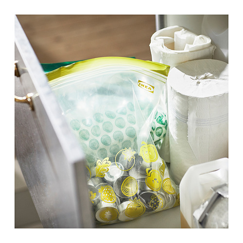 Una bolsa de almacenamiento transparente abierta de Ikea, verde y amarilla, que contiene varios artículos pequeños junto a panecillos blancos.