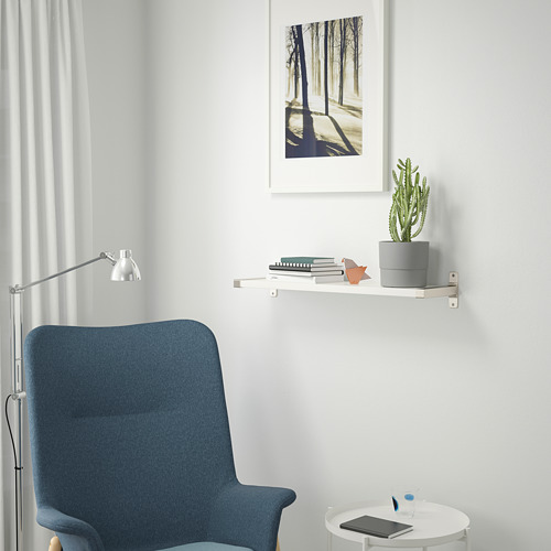 Rincón minimalista con silla azul, mesa para portátil y estantería alta con cactus y cuadro.