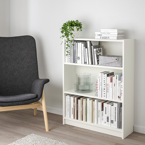 Estantería blanca BILLY con 3 estantes, con capacidad para libros, vela y planta. Silla gris al lado, encaja perfectamente en la esquina.