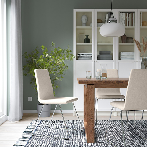 Comedor moderno con silla LILLÅNÄS beige, mesa de madera, lámpara colgante blanca, alfombra gris y estantería con jarrón azul.