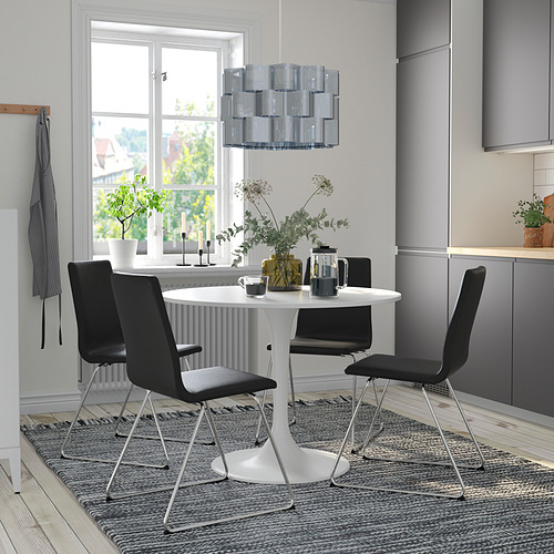 Moderno juego de comedor con mesa DOCKSTA blanca y sillas negras, rodeado de una decoración gris, cerca de un gran ventanal.