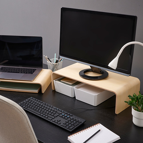Soporte de monitor de madera con computadora portátil, almacenamiento para teclado, sobre escritorio oscuro. Incluye lámpara, planta, teclado inalámbrico y bloc de notas para un espacio de trabajo eficiente.