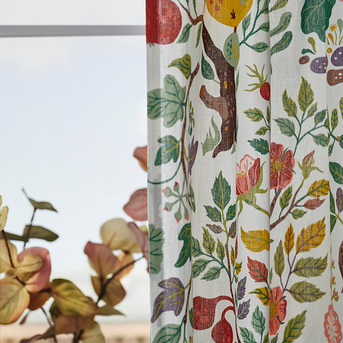 Brillantes cortinas florales cuelgan de una ventana, filtrando la luz con diseños vibrantes. Una planta se encuentra en primer plano, realzando la decoración de las habitaciones.