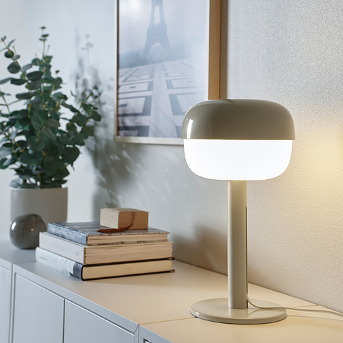 Lámpara de mesa moderna BLÅSVERK, luz suave, diseño elegante. Tono verdoso, forma dulce, pequeño, al lado de libros, planta, cuadro.