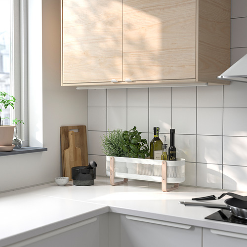 Una moderna encimera de cocina con organizador RISATORP, tablas de cortar, plantas y botellas. El organizador blanco con patas de abedul sujeta los objetos de forma ordenada.