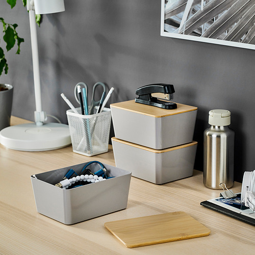 La caja gris de KUGGIS almacena artículos de oficina azules/blancos, hechos de plástico reciclado, se mezclan con accesorios de escritorio.