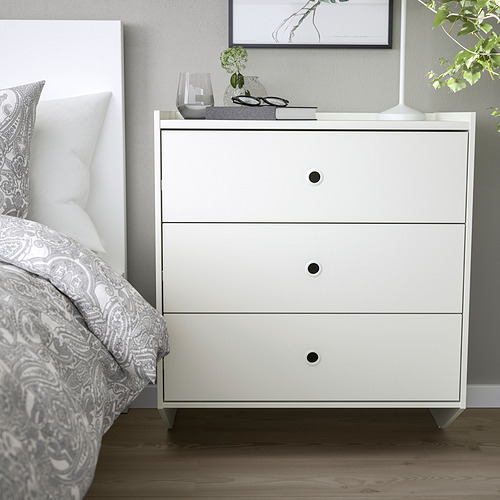 Cofre RACKNÄS blanco minimalista junto a la cama. Tres cajones, diseño elegante, pequeño y práctico.