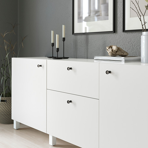 Mueble blanco con pomos negros, con acabado antracita y detalles redondeados. La parte superior contiene candelabros y artículos de decoración.