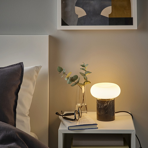 Elegante dormitorio con lámpara MOLNART, plantas, libro y arte abstracto.