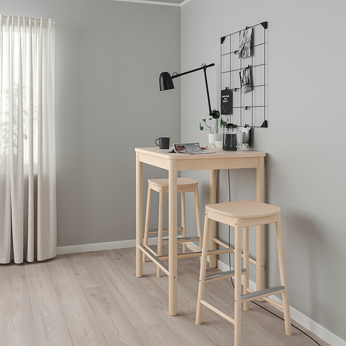 Pequeña mesa de bar RÖNNINGE de madera clara con taburetes en esquina de habitación minimalista, cortina blanca, pared gris, lámpara negra.