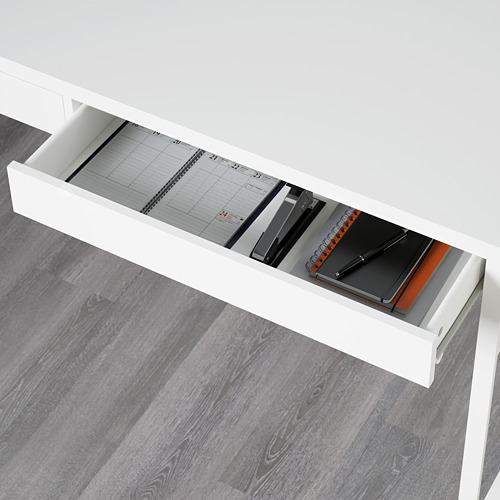 Cajón de escritorio blanco abierto que revela cuadernos y planificador. La superficie reflectante en el interior de la parte posterior muestra el equipo de oficina.