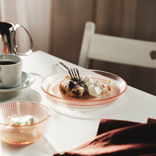 Un postre emplatado con crema batida junto a una taza de café y una jarra sobre una mesa blanca.