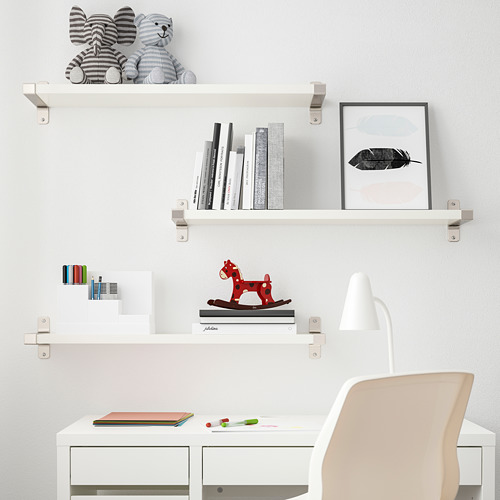 Tres estantes blancos de BERGSHULT exhiben juguetes, libros y arte, sobre un escritorio blanco con una silla beige.