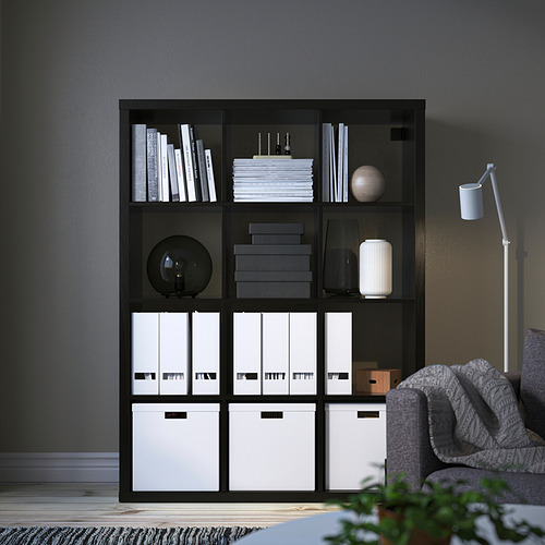 Estante negro KALLAX: alto, con varios compartimentos, que contiene libros y decoración.