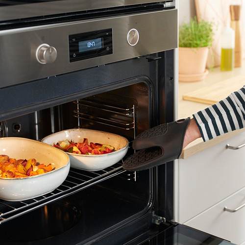 Persona que usa un guante de cocina de silicona para sacar los platos del horno. El guante protege las manos y proporciona agarre.