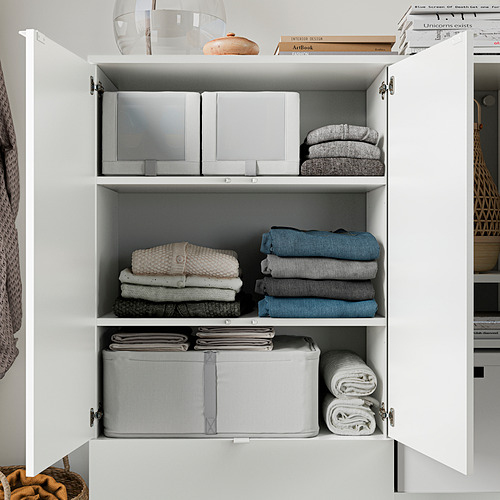 Armario organizado con estantes blancos, ropa cuidadosamente doblada y artículos decorativos.