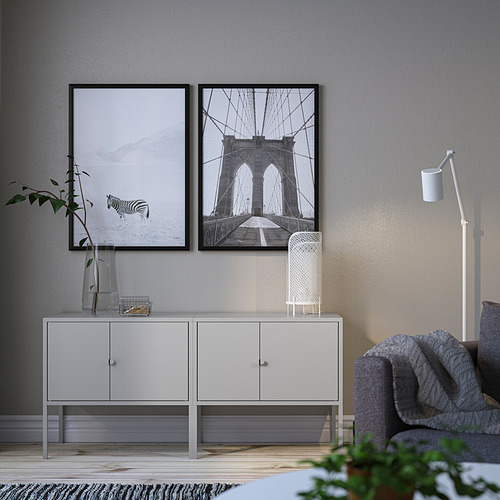 Sala de estar moderna con gabinete blanco LIXHULT, dos fotos enmarcadas, silla acolchada gris, lámpara blanca y plantas.