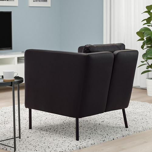 Moderno sillón oscuro con cojín de respaldo móvil, sobre elegantes patas de metal, en un ambiente acogedor.