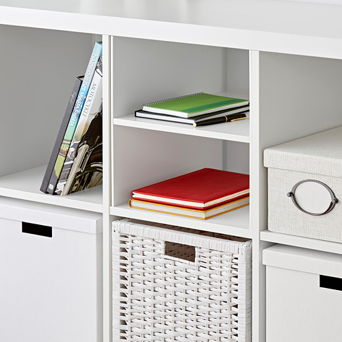 Estantería KALLAX blanca con libros, cesta y caja de almacenaje. Los libros están cuidadosamente organizados en los estantes.