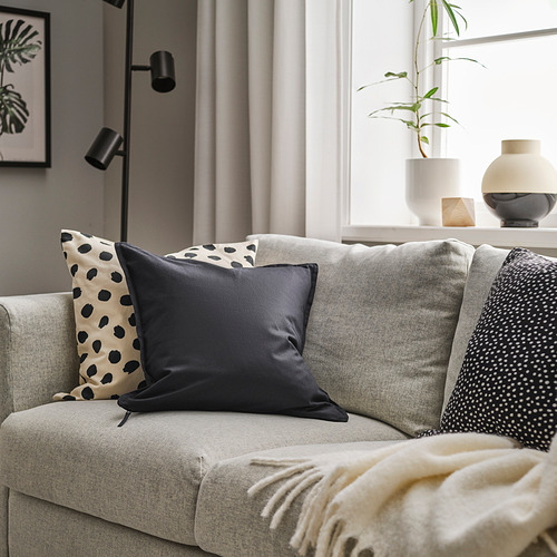 Sala de estar moderna con GURLI, un cojín de algodón negro, sobre un sofá gris, complementado visualmente con almohadas estampadas y una acogedora manta.