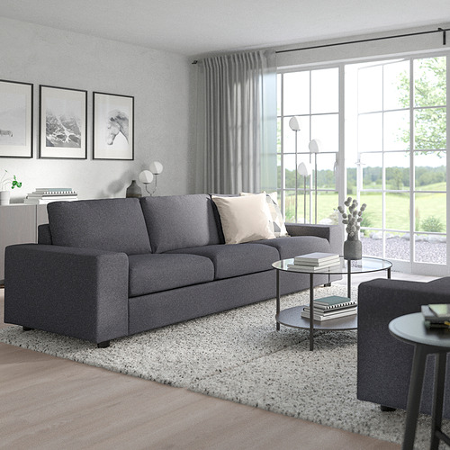 Moderno conjunto de sofás VIMLE gris, grande, con dos sofás, sillas, mesa de centro de cristal, alfombra, lámparas, plantas, frente a grandes ventanales con cortinas.