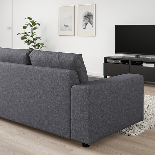 Sala de estar moderna con sofá gris VIMLE, suelo de madera, paredes blancas, televisión, planta y arte enmarcado. El sofá parece más grande que el soporte de televisión.