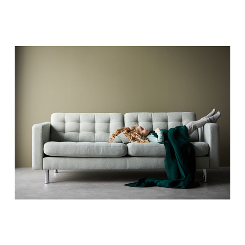 Persona durmiendo en un sofá acolchado gris claro con manta verde, piernas levantadas, diseño moderno, espacio habitable acogedor.