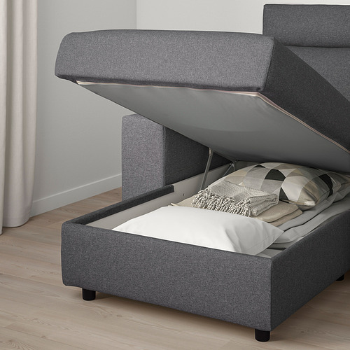 Sofá tapizado gris con compartimento de almacenamiento abierto, mostrando almohadas en su interior.