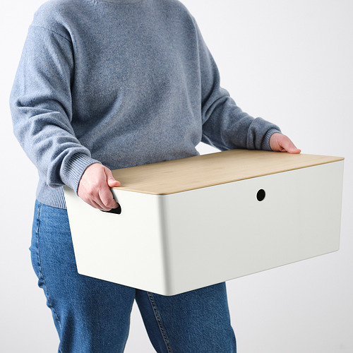 Persona que lleva una caja de almacenamiento grande con tapa y asa. Ideal para juegos familiares o pasatiempos, se adapta a los estantes de bestå.