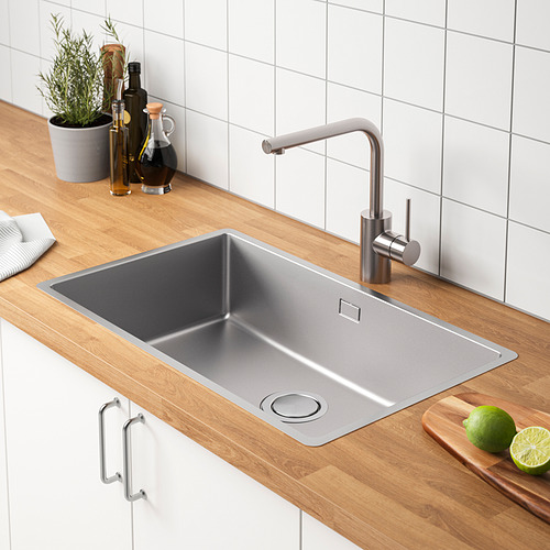 Fregadero de cocina de acero inoxidable con grifo, colocado sobre encimera de madera. Junto a una tabla de cortar con limas y junto a los condimentos.