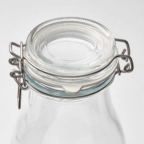 Un frasco de vidrio transparente con una abrazadera de metal segura y un sello de goma, ideal para conservar y almacenar alimentos.