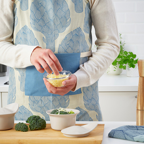 Persona en delantal ralla queso en la cocina con brócoli en la encimera.