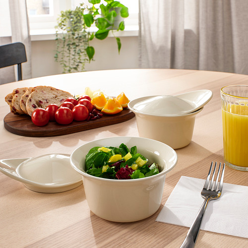 Mesa puesta con comida: un plato de ensalada, pan, frutas y zumo de naranja. Un plato de cerámica blanca, probablemente para hornear y servir, está presente en la mesa.