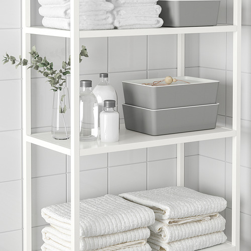 Estantería blanca con toallas blancas cuidadosamente apiladas y compartimentos de almacenamiento, incluida la caja KUGGIS gris para organizar artículos de baño o escritorio.