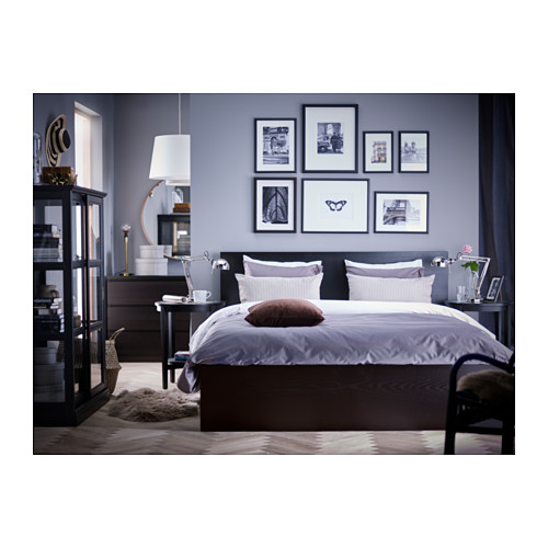 Dormitorio moderno con cama MALM gris, sábanas moradas, muebles oscuros y galería de arte en la pared.